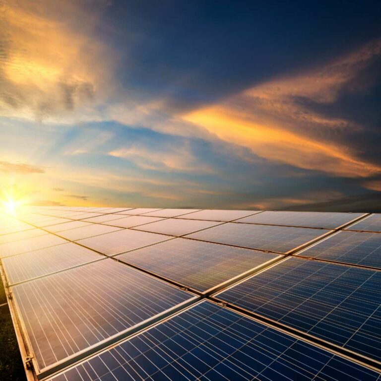Solar panels with a sunset shining on them against a blue sky and clouds background.