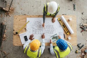 Three construction workers around a table looking at a building plan.