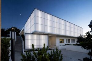 A modern house with white polycarbonate windows in a night time setting with the moon in the background.